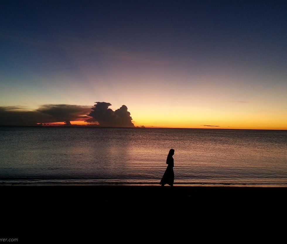 A lady in silhouette walking along the beach shore under the sunset